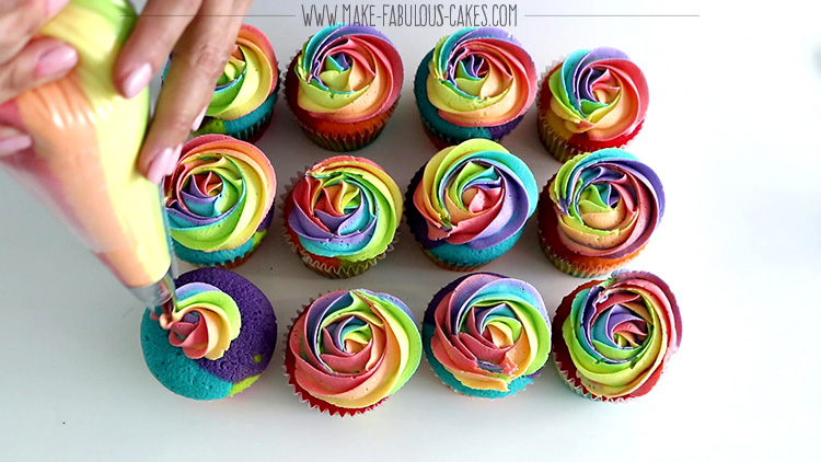 piping rainbow frosting over rainbow cupcakes